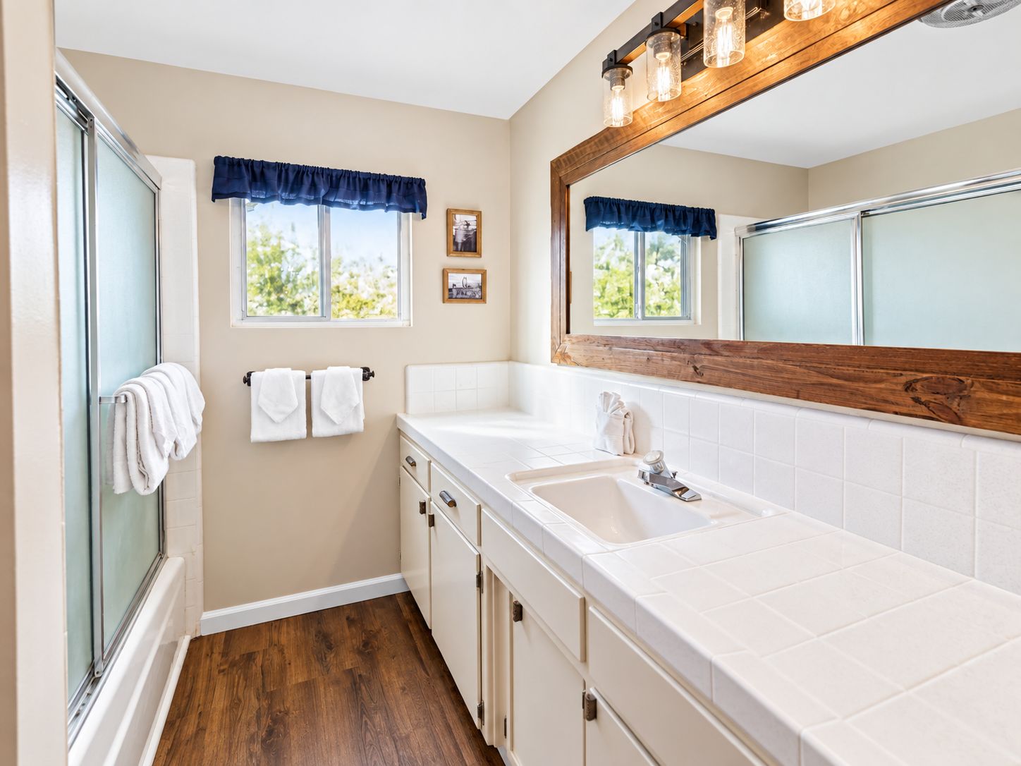 A bathroom with a walk-in shower, two sinks, wooden vanity, and a large mirror.