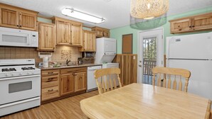 Una cocina con armarios de madera, estufa, microondas y una mesa de comedor con sillas.