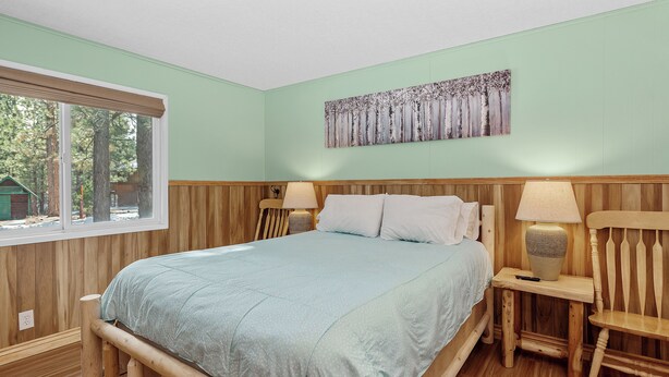 Un dormitorio con estructura de cama de madera, un ventanal grande y un cuadro en la pared.