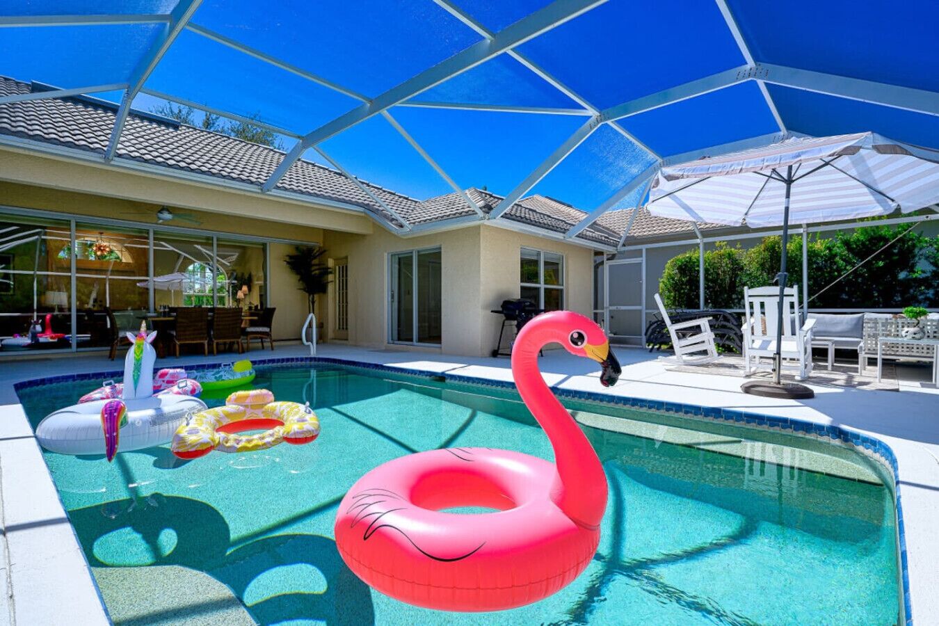 En swimmingpool med en lyserød flamingo-svømmebøje, omgivet af liggestole og parasoller.