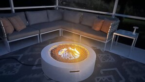 A modern outdoor seating area with a circular fire pit, a gray sofa with cushions, and a small table.