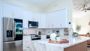 A modern kitchen with white cabinetry, stainless steel appliances, and a marble island.