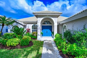 Stucco-clad home with arched windows and a decorative entrance, set amidst a lush garden with a palm tree.