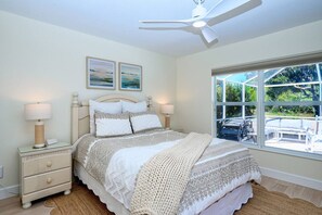 Relax in this serene bedroom with a large bed, nightstand, and ceiling fan, offering a peaceful view of the outdoor area with lush greenery.