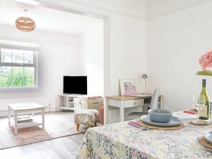 A bright room with a television, desk, chair, and a dining table with a floral tablecloth.