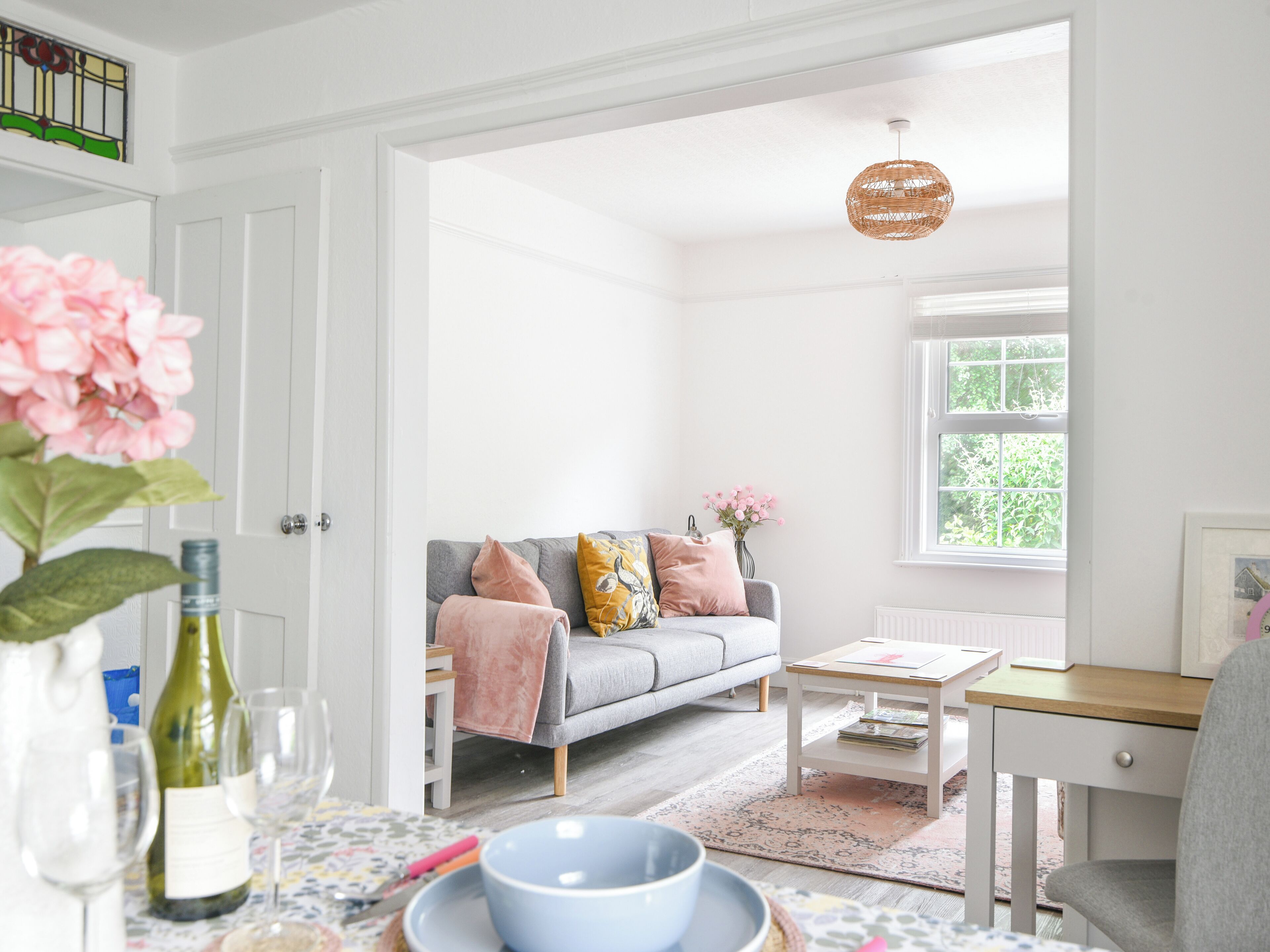 A bright living room with a grey sofa, a small table, and a window with a view of greenery.