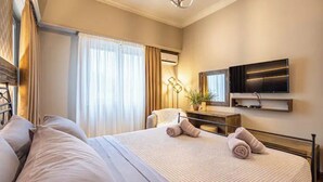 A hotel room with a large bed, a flat-screen TV mounted on the wall, a desk with a lamp, and a window with curtains. - Periklis luxury apartment 3 (Athina)