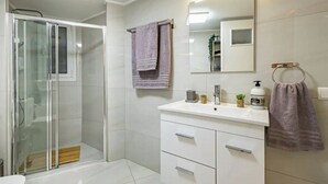 A modern bathroom with a glass shower enclosure, white vanity with drawers, a large mirror, and a towel rack. - Periklis luxury apartment 3 (Athina)