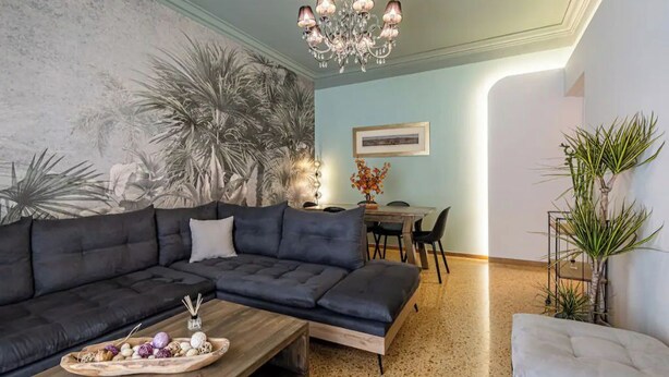 A living room with a sectional sofa, a wooden coffee table, a chandelier, and a dining area with a table and chairs. - Periklis luxury apartment 3 (Athina)