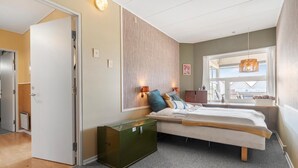 Een slaapkamer met een bed, nachtlampjes, een groen kastje en een raam met uitzicht.