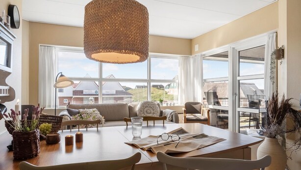 Een ruime woonkamer met een grote eettafel, comfortabele zithoek en uitzicht op de omgeving door grote ramen.