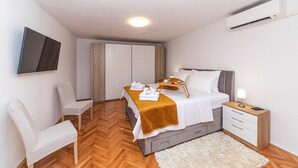 A modern hotel room with a bed, a bedside table, a chair, a wardrobe, and an air conditioning unit.