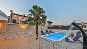 A swimming pool with lounge chairs, a palm tree, and a stone wall.