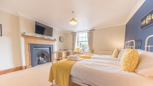 A bedroom with two beds, a fireplace, a TV, and a window with curtains. - Abbey Farm House (St Bees)
