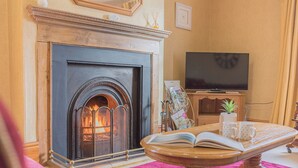 A cozy living room with a fireplace, a television, and a coffee table with books and mugs. - Abbey Farm House (St Bees)