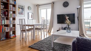Una sala de estar moderna con comedor, una estantería, un televisor de pantalla plana y un ventanal con cortinas.