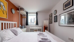 Una habitación de hotel con cama, escritorio, silla, armario y ventana con cortinas.