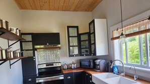 Une cuisine moderne avec des meubles noirs, des appareils en acier inoxydable et un plafond en bois.