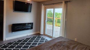 Une chambre dotée d’un ventilateur de plafond, d’un téléviseur fixé au mur, d’une porte-fenêtre coulissante donnant sur une terrasse et d’un tapis à motifs.