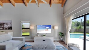 En moderne stue med et fladskærms-tv, en sofa, et sofabord og udsigt til en swimmingpool.