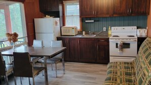 A compact kitchen with wooden cabinets, a dining table with chairs, a microwave, a stove, and a window with blinds. - Villa Dave (Gracefield)