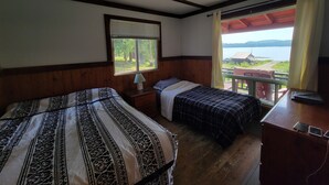 A room with two beds, a window with blinds, a lamp, and a view of a lake and mountains. - Villa Dave (Gracefield)
