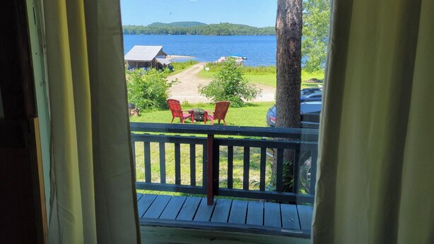 A wooden deck with a railing, overlooking a lake with a dock and a small building. - Villa Dave (Gracefield)
