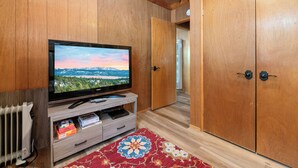 A wooden-paneled room with a television on a wooden stand, a radiator, a patterned rug, and a wardrobe. - Finch Nest (Big Bear Lake)