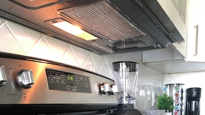 Et køkken med komfur, kaffemaskine og blender på bordet.