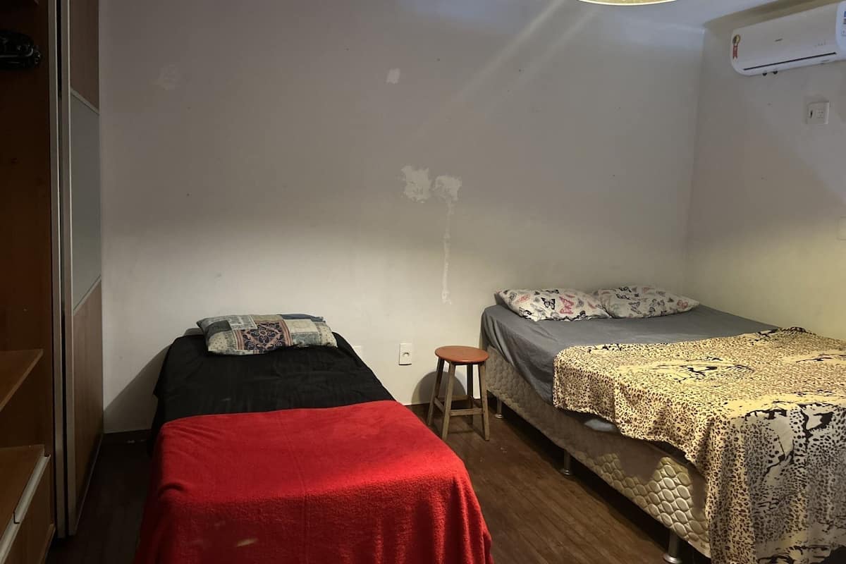 A small, compact room with two single beds, a small stool, and a ceiling light.