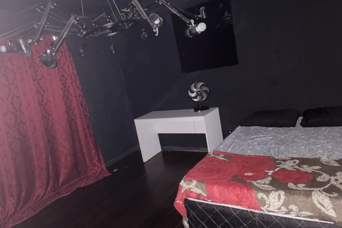 A bedroom with a bed, a nightstand, a wall-mounted lamp, and a ceiling fan.