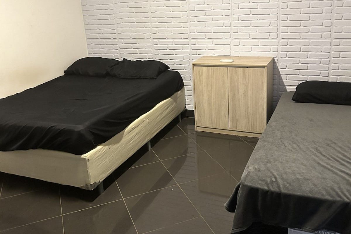 A bedroom with two beds, a wooden nightstand, and a white brick-patterned wall.