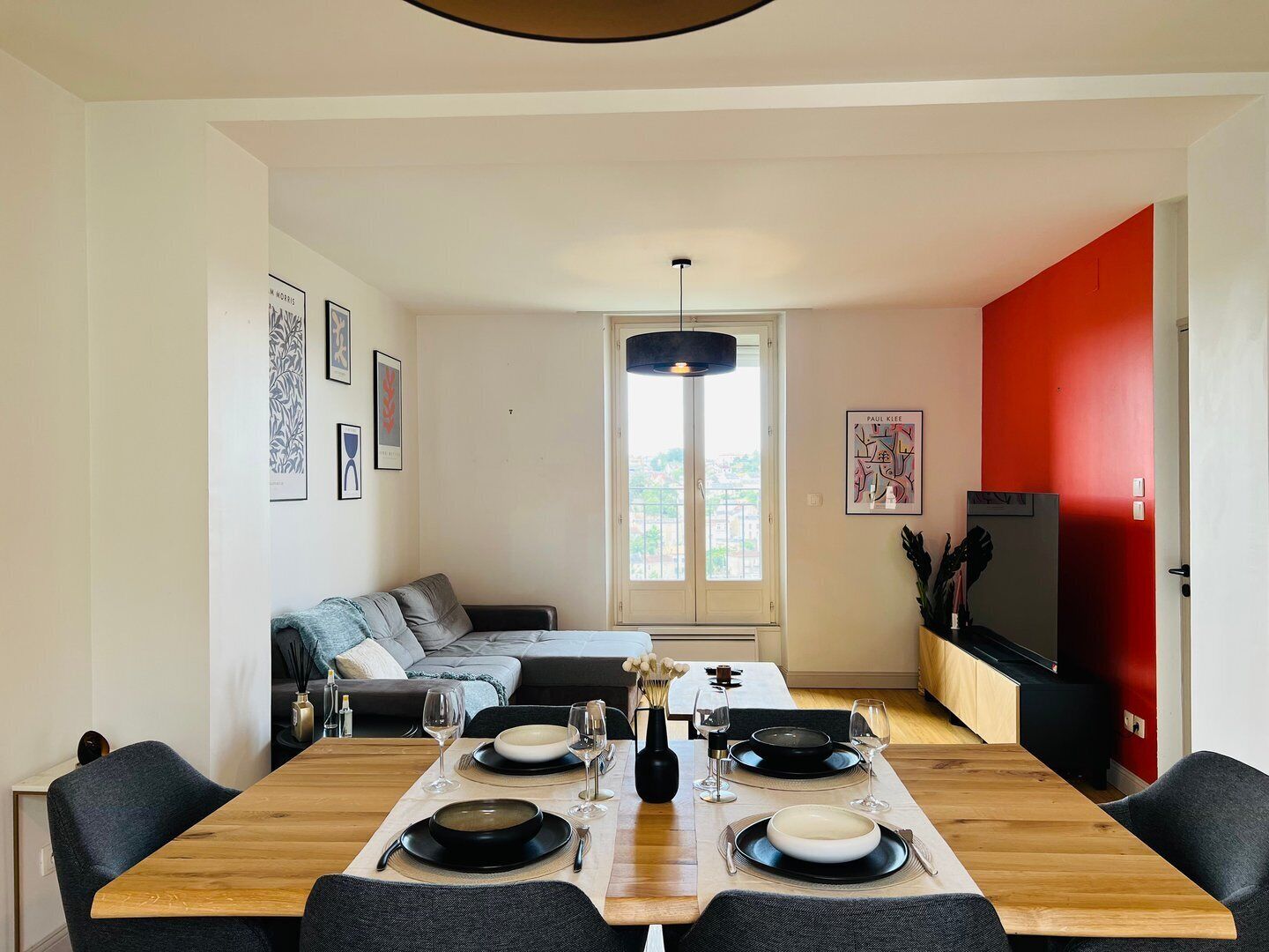 Uma sala de jantar moderna com uma mesa de madeira posta para quatro pessoas, um sofá e uma parede em destaque na cor vermelha.