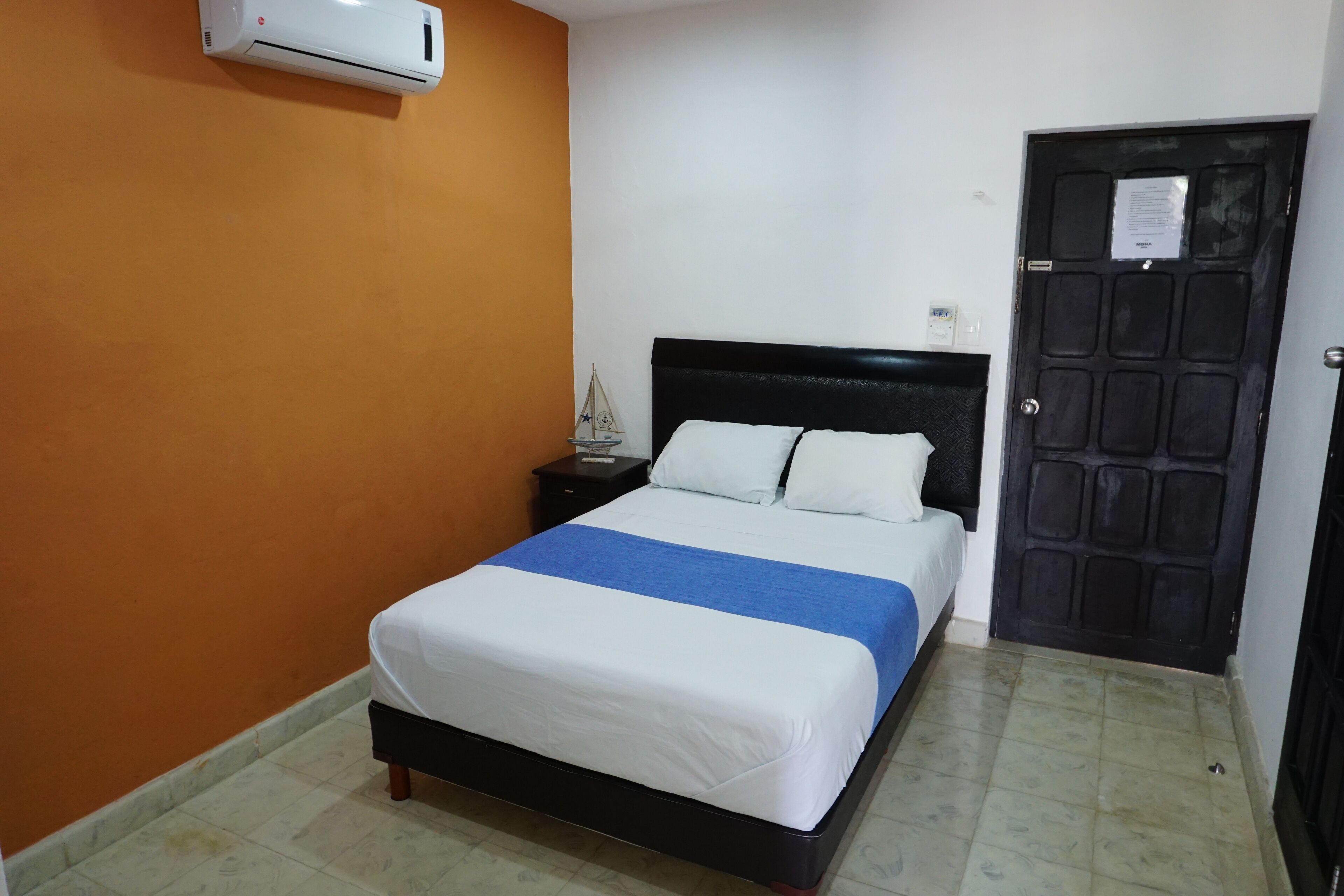 Ein Hotelzimmer mit Bett, Nachttisch, Klimaanlage und Tür.