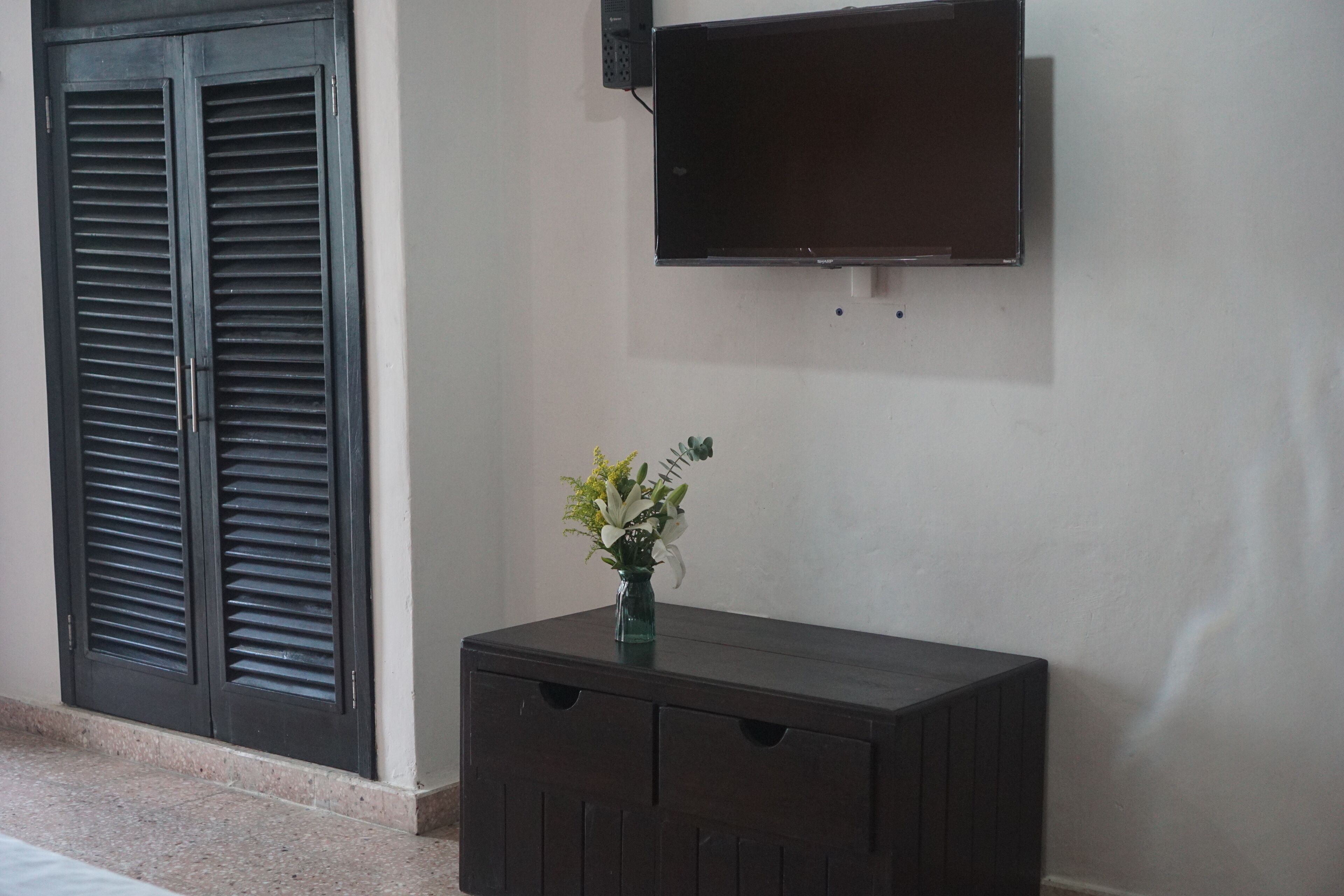 A room with a dark wooden cabinet, a small vase with flowers, and a mounted television on the wall.