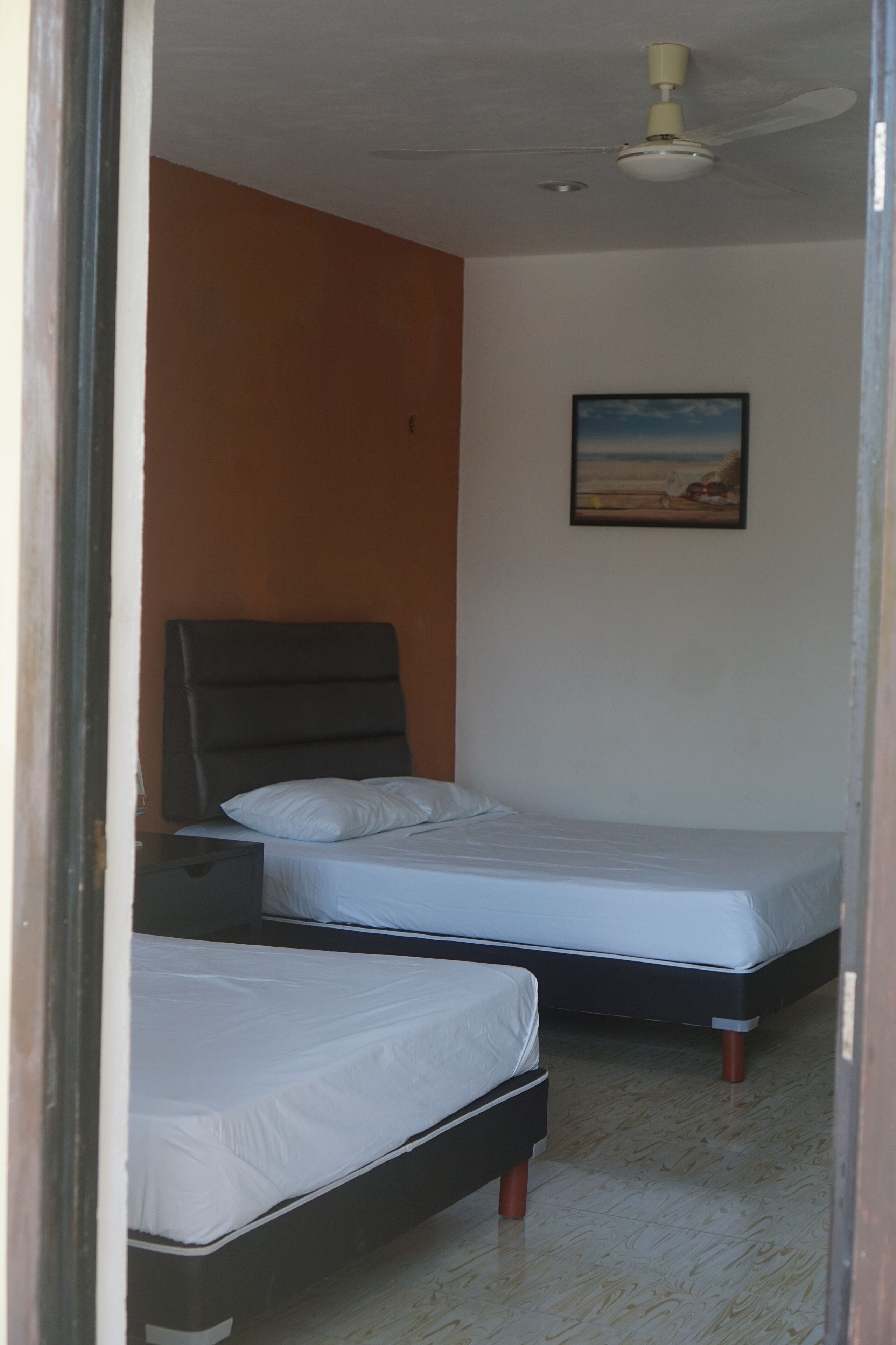 Une chambre avec deux lits, un ventilateur de plafond et un tableau au mur.