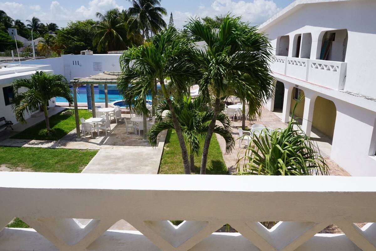 A pool area with palm trees, outdoor seating, and a white building with balconies.