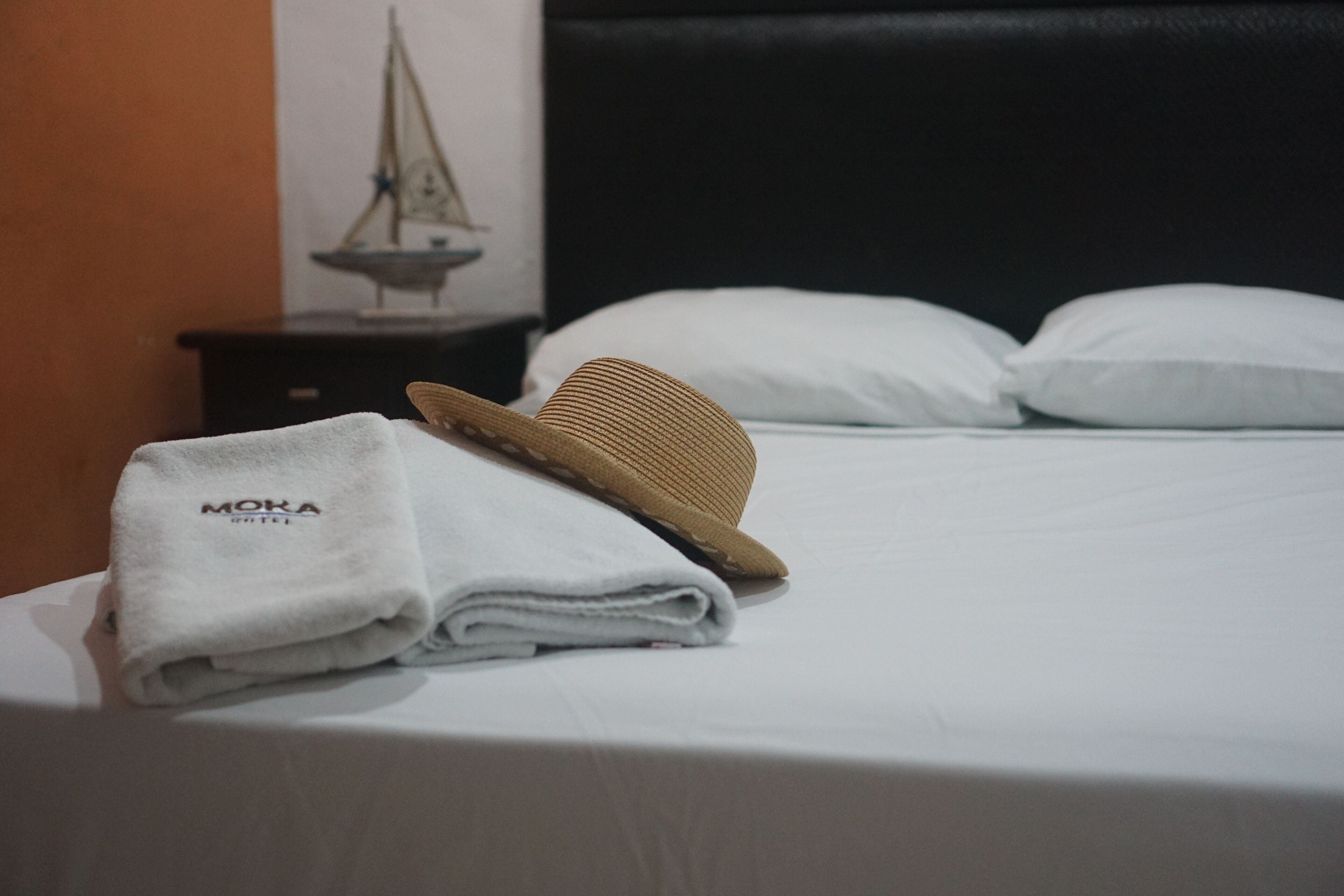 A neatly made bed with a folded white towel and a straw hat on top.