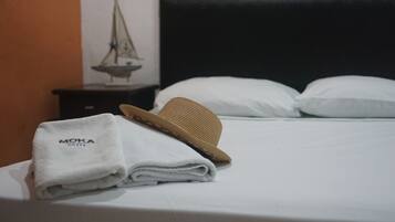 A neatly made bed with a folded white towel and a straw hat on top.