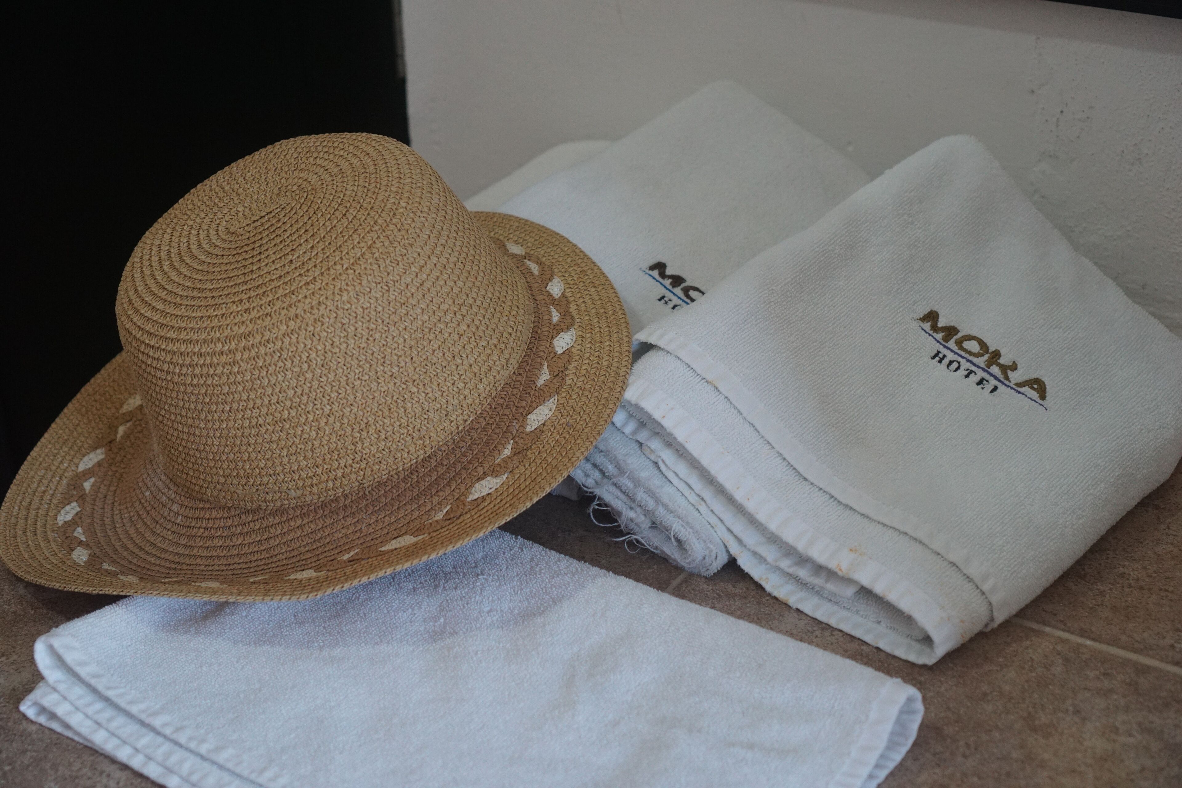 A straw hat, folded towels, and a white cloth with "MOKA HOTEL" text.