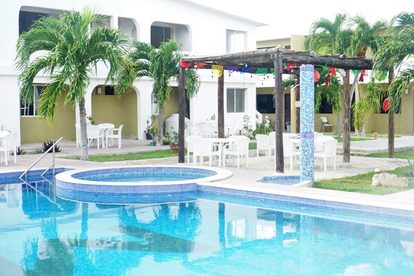 A swimming pool with a tiled edge, surrounded by palm trees and white chairs.