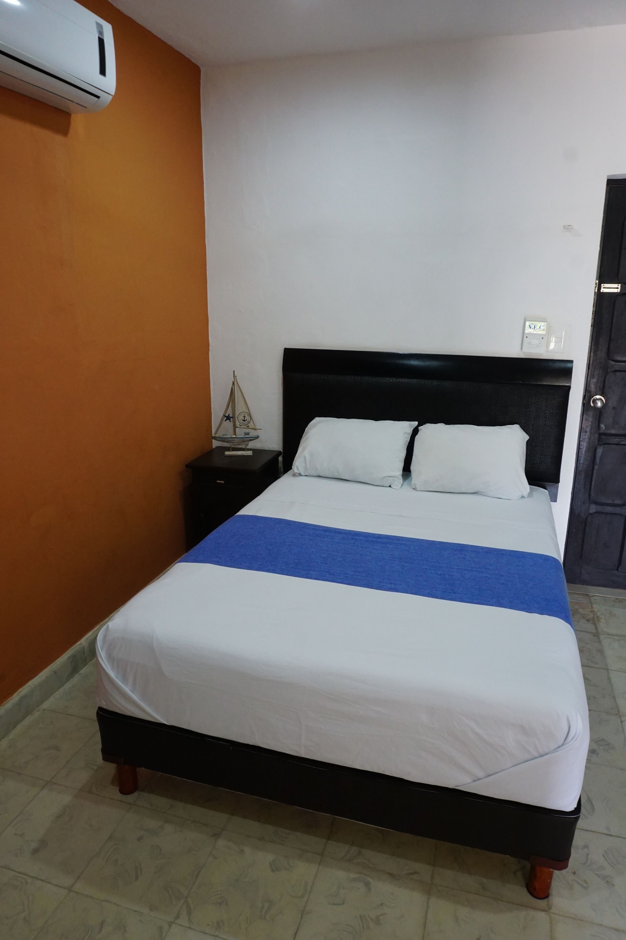 A bed with a white and blue bedspread, a black headboard, and a small table with a decorative item beside it.