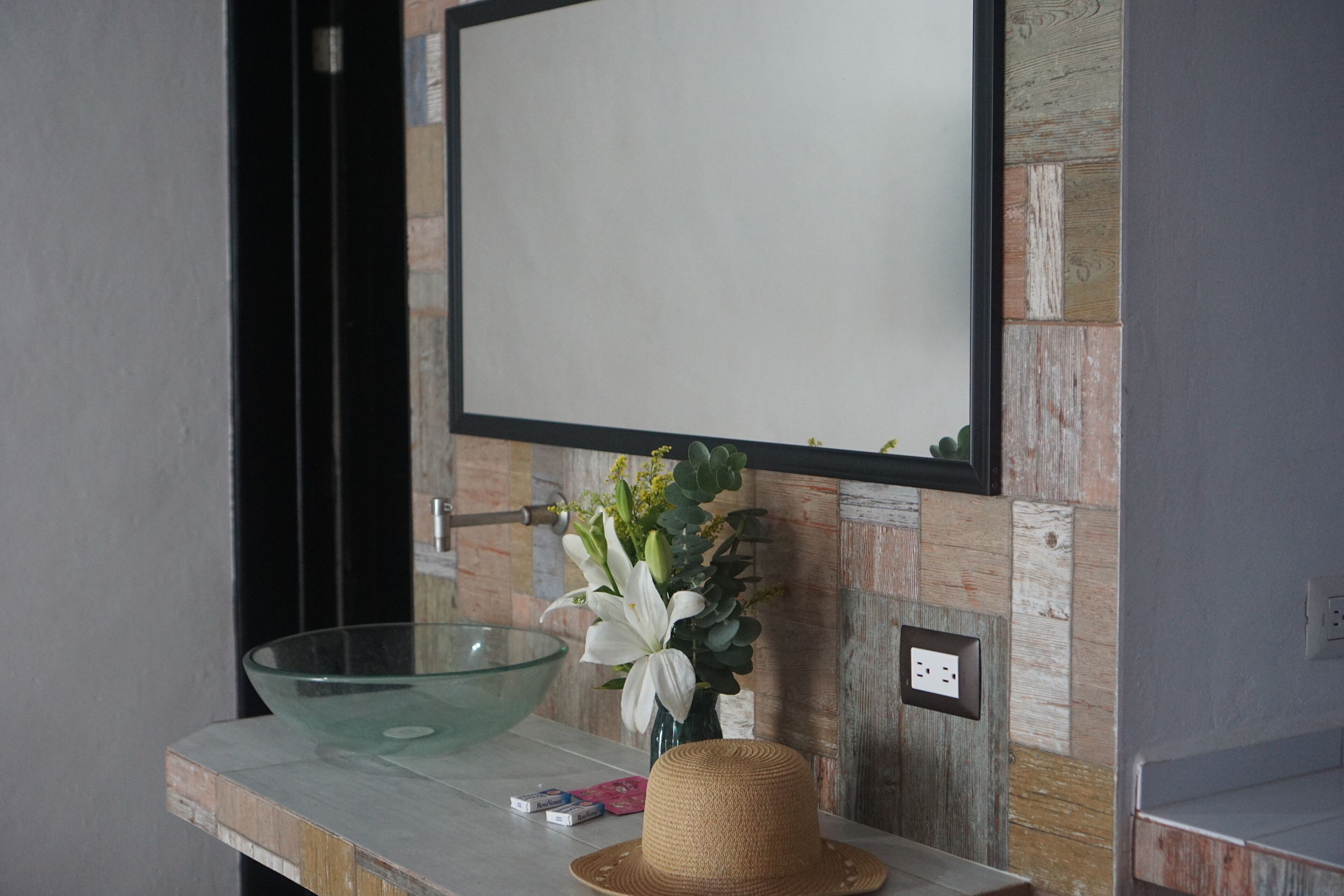 A bathroom with a glass bowl sink, a vase with flowers, and a straw hat on the counter.