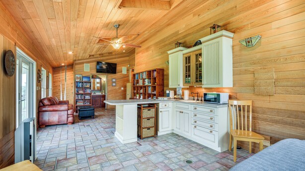 A cozy cabin interior with a wooden ceiling, a central island with a microwave, a leather sofa, and a bookshelf. - Spacious Lowville Retreat on 4 Private Acres! (Lowville)