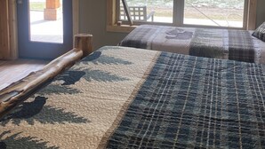 Ein Schlafzimmer mit großem Fenster, das auf einen Fluss und Grünblicke blickt. Eine Holztür und ein Bett mit gemustertem Überwurf sind zu sehen.