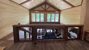 Ein geräumiges Zimmer mit Holzwänden und -decke, einer hohen Decke mit geneigtem Dach und einem großen Fenster mit Blick ins Grüne.