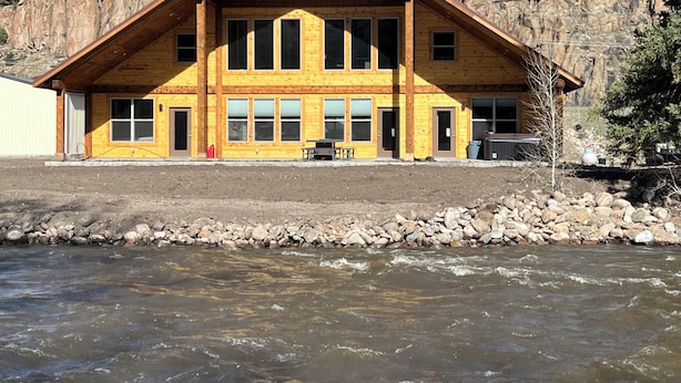Eine Lodge mit einer großen Holzkonstruktion, mehreren Fenstern und Blick auf einen Fluss.