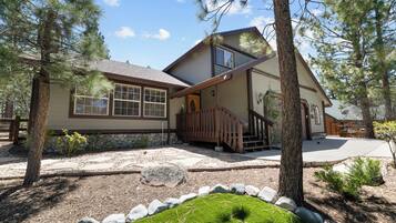 A two-story house with a stone foundation, wooden deck, and a stone pathway leading to the entrance.