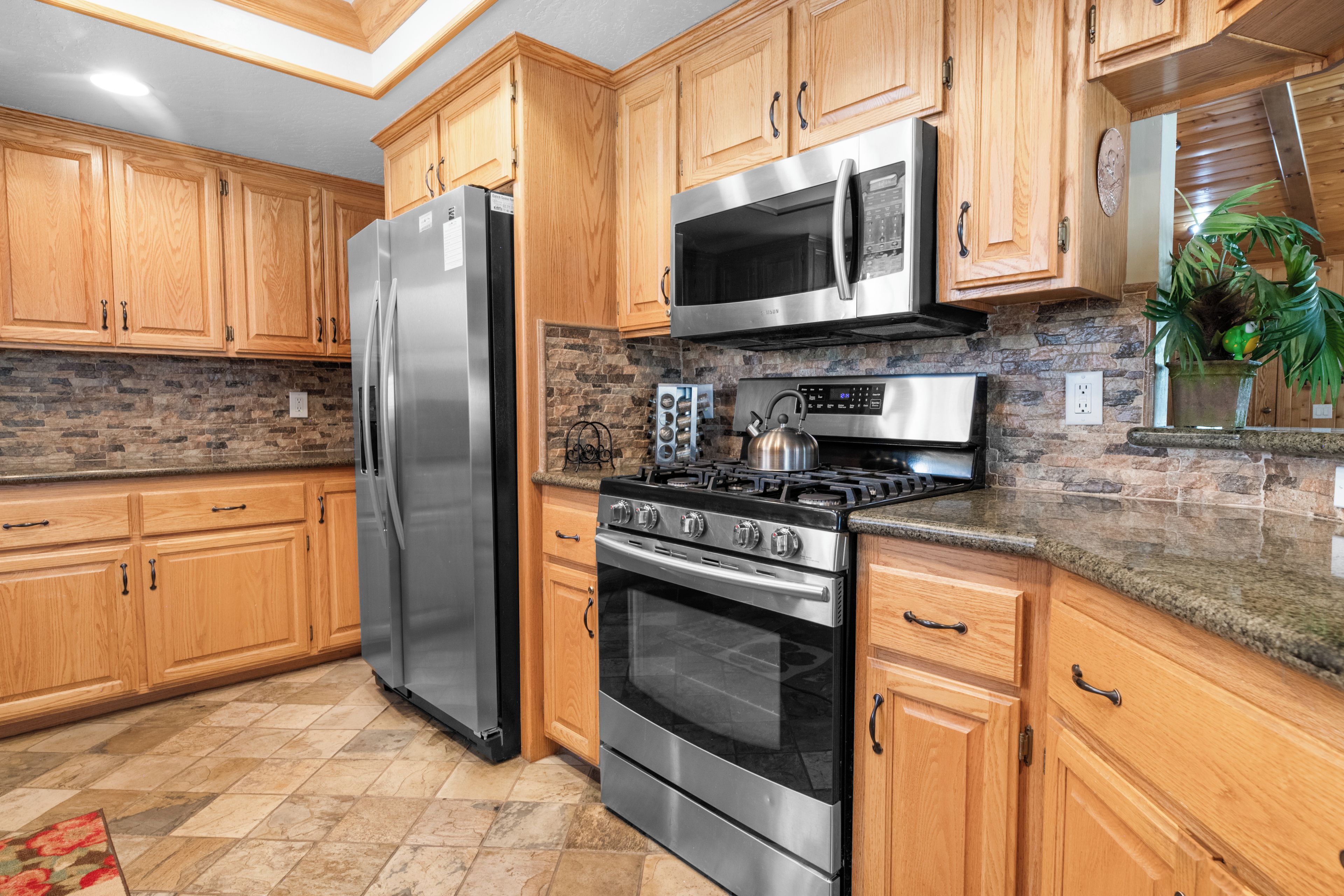 Una cocina con armarios de madera, un refrigerador de acero inoxidable, un microondas, una estufa y un respingo de azulejos.