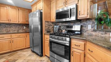 A kitchen with wooden cabinets, a stainless steel refrigerator, a microwave, a stove, and a tiled backsplash.
